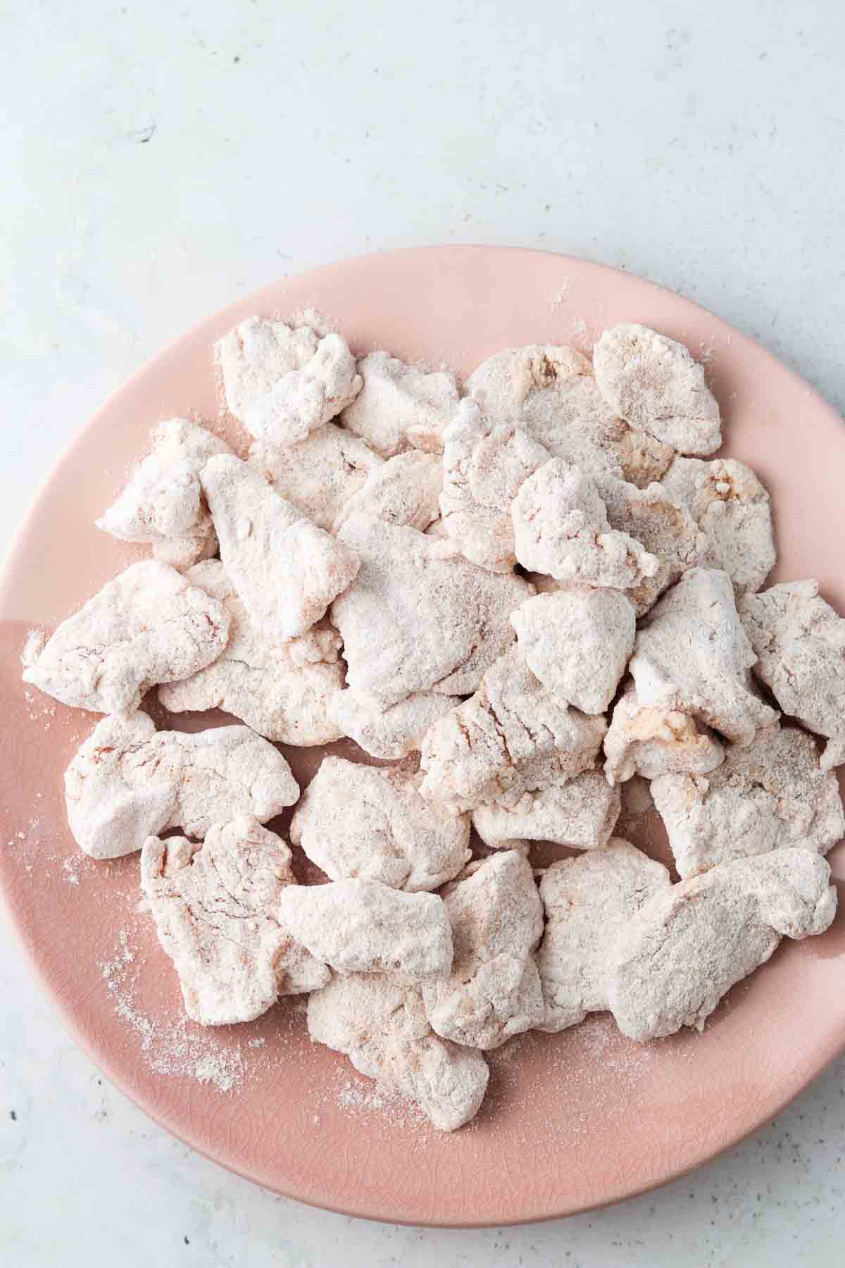 Cubbed chicken breast coated in flour on a pink plate.