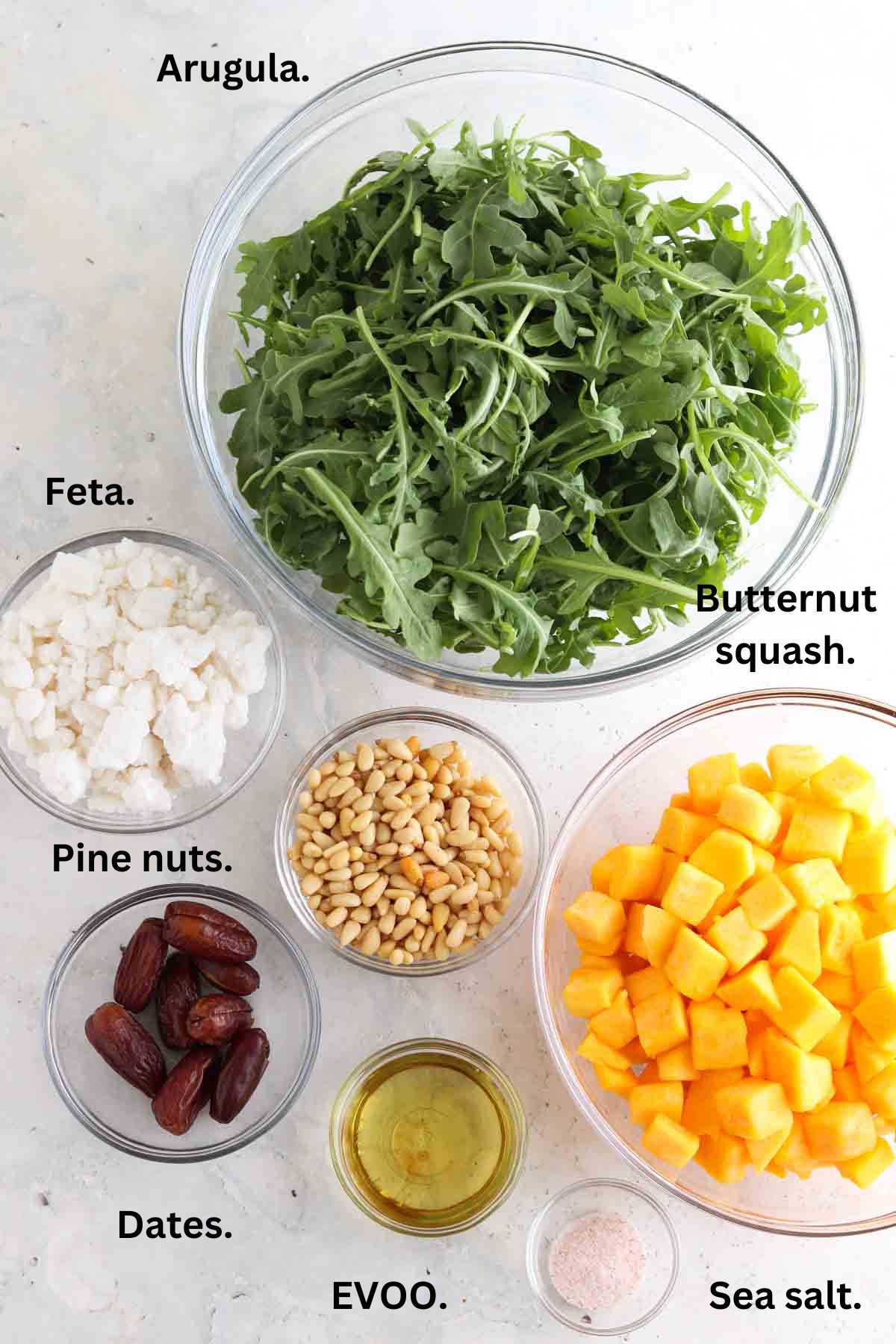 Arugula, goat cheese, squash, dates, olive oil, and pine nuts laid out on the counter.