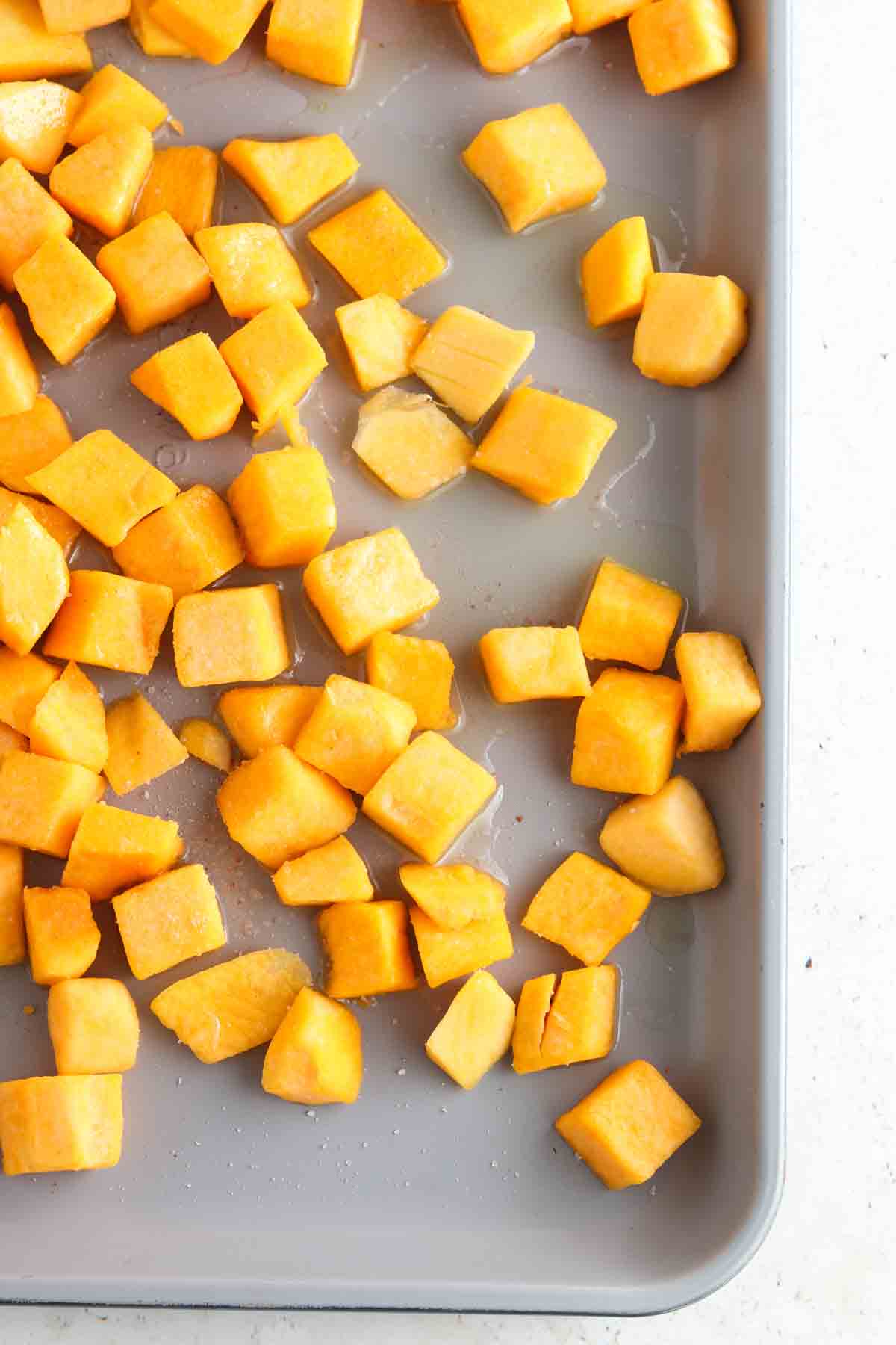 Butternut squash on a sheet pan laid out with sea salt and olive oil.