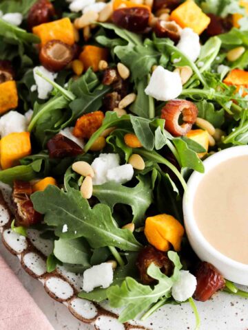 Arugula salad with squash, feta sheet, pine nuts and dates on a plate.