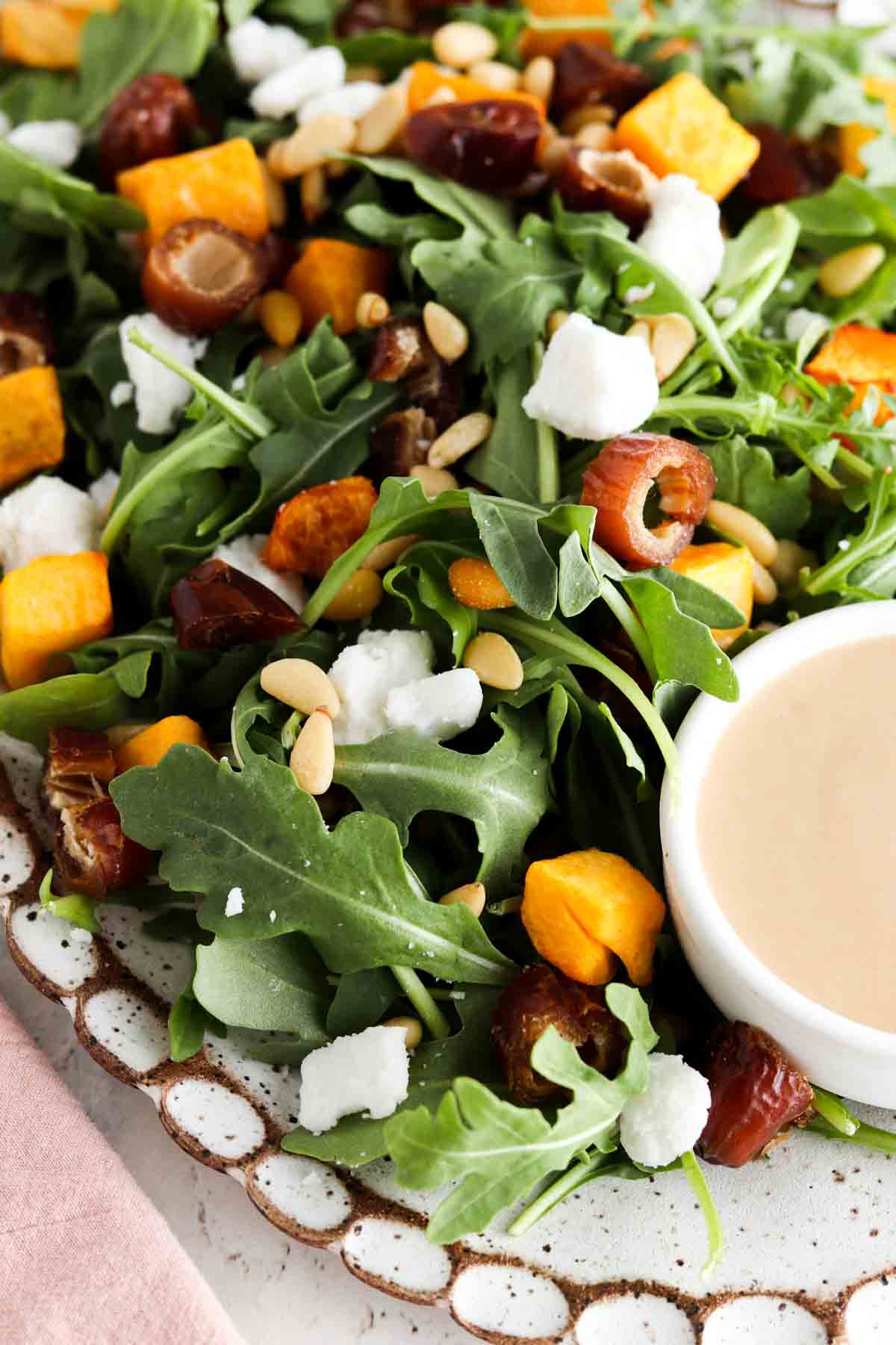 Plate of arugula, butternut squash, dates, pine nuts and feta sheet.