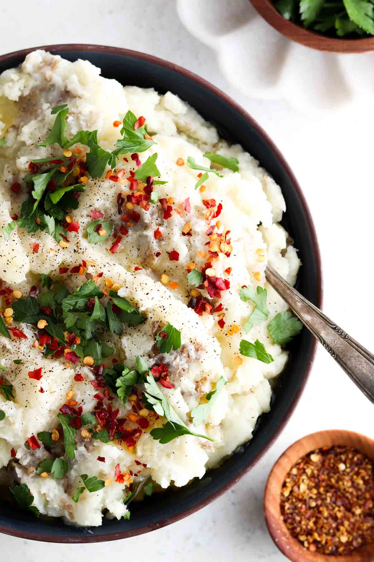 Mashed potatoes in a bowl with gravy, fresh herbs and red pepper flakes on top.