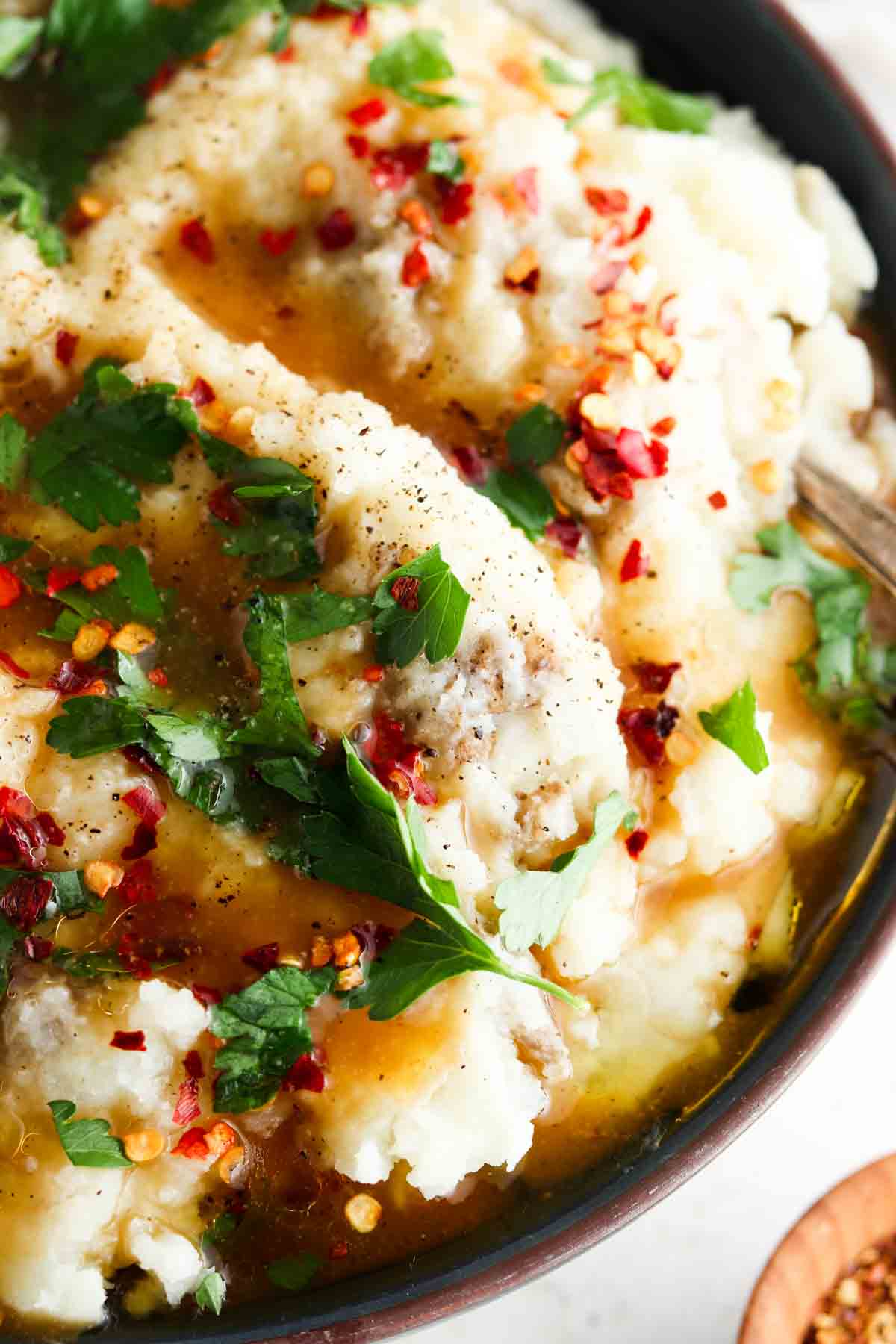 Mashed potatoes in a bowl with gravy, fresh herbs and red pepper flakes on top.