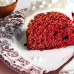 Slice of red velvet cake on a plate with white chocolate on top of the icing.