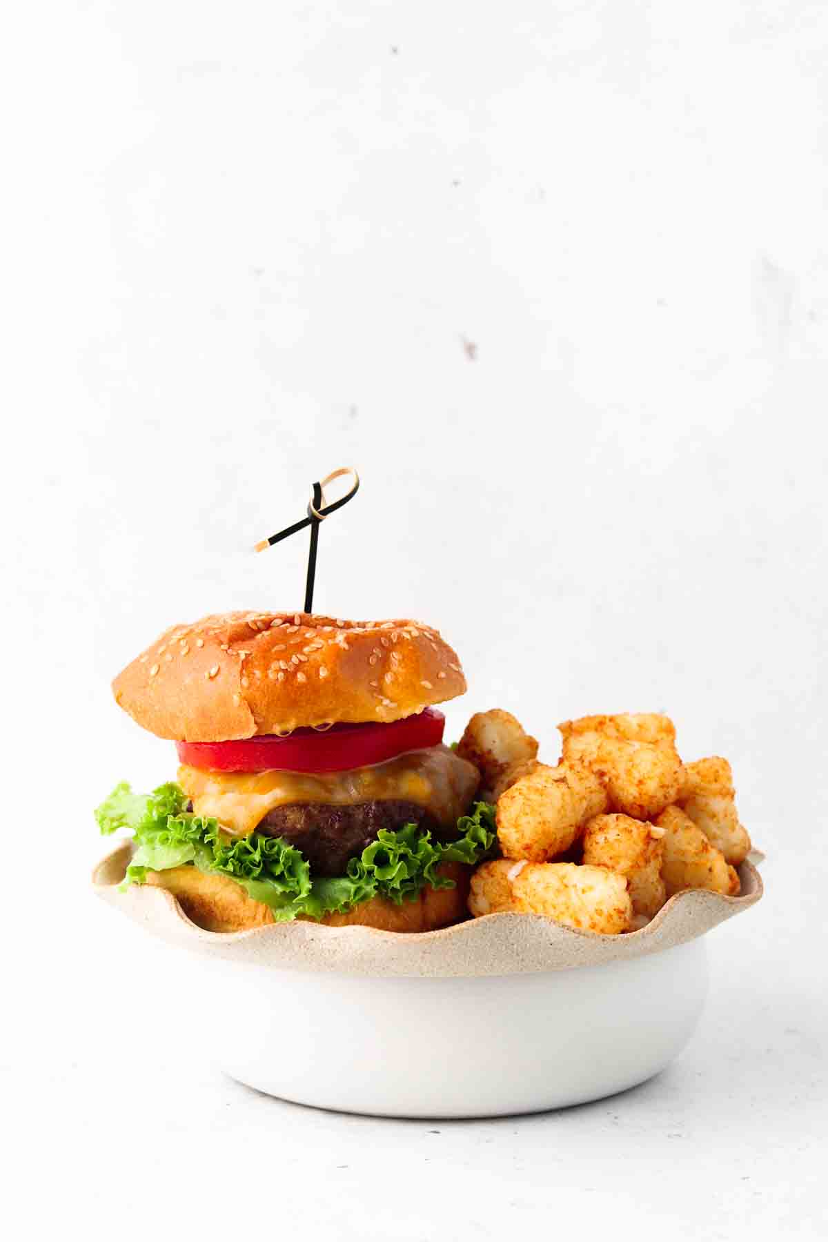 A gluten free burger on a plate with tater tots.