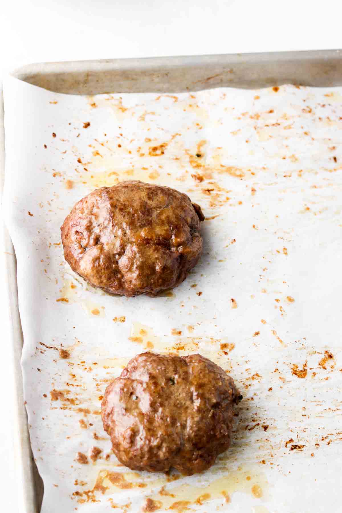 Baked beef burger patties on a baking sheet.