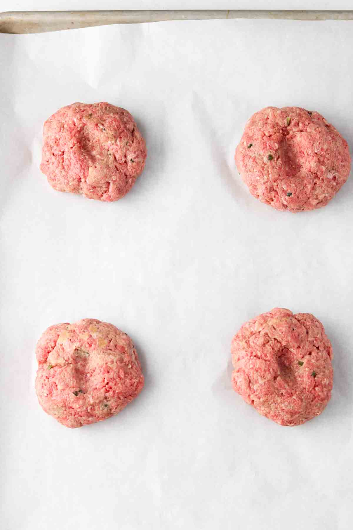 Raw beef burger patties on a baking sheet.