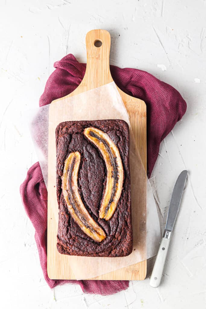 whole chocolate banana bread on a wooden tray with a knife