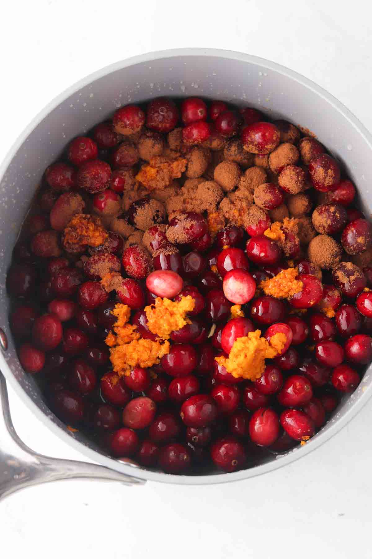 Fresh cranberries, orange zest, orange juice and dates in a pot.