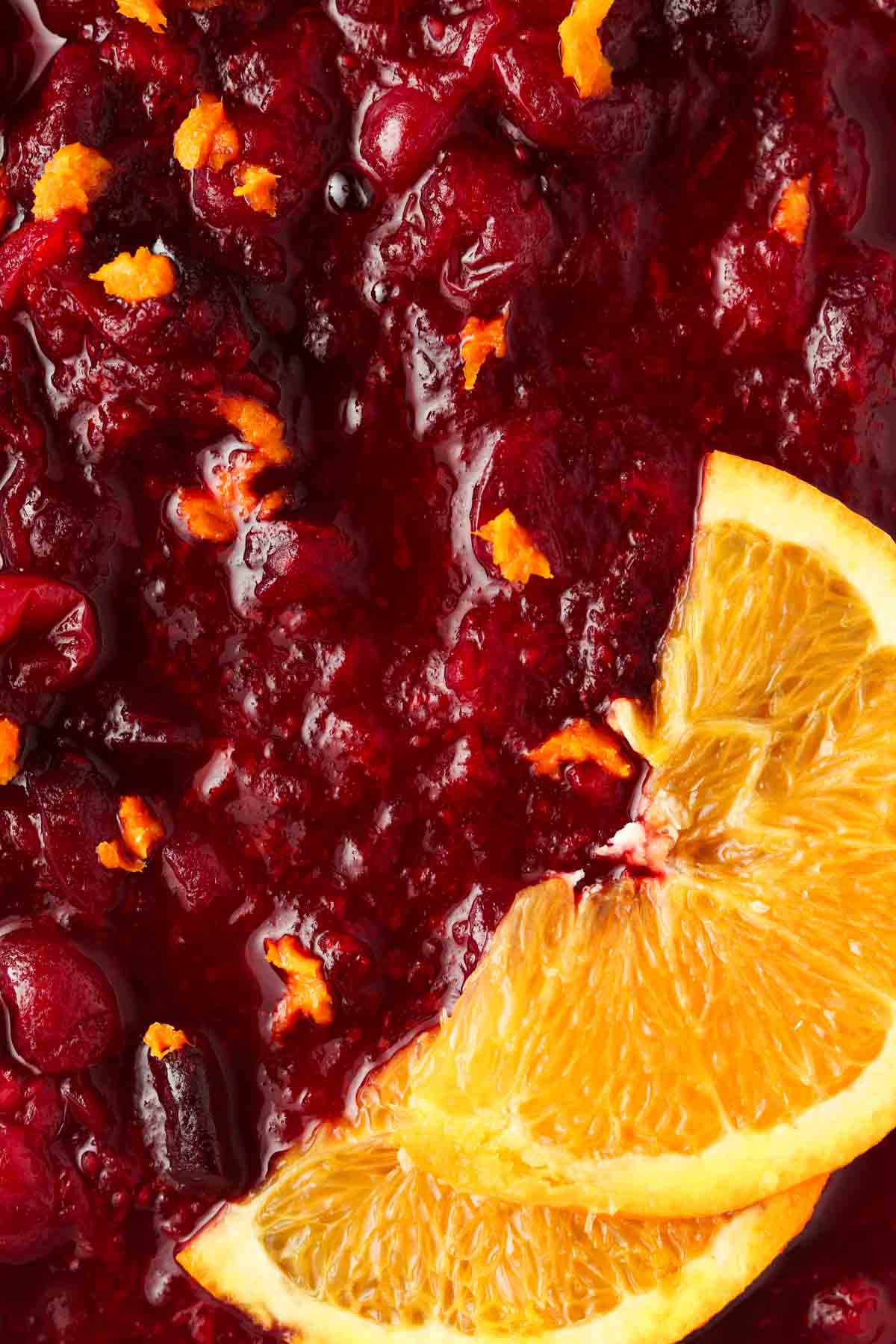 Close up photo of cooked cranberry sauce in a casserole dish with orange zest and orange sliced on top.