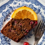 Piece of gluten free orange cake on a plate with an orange slice on top.