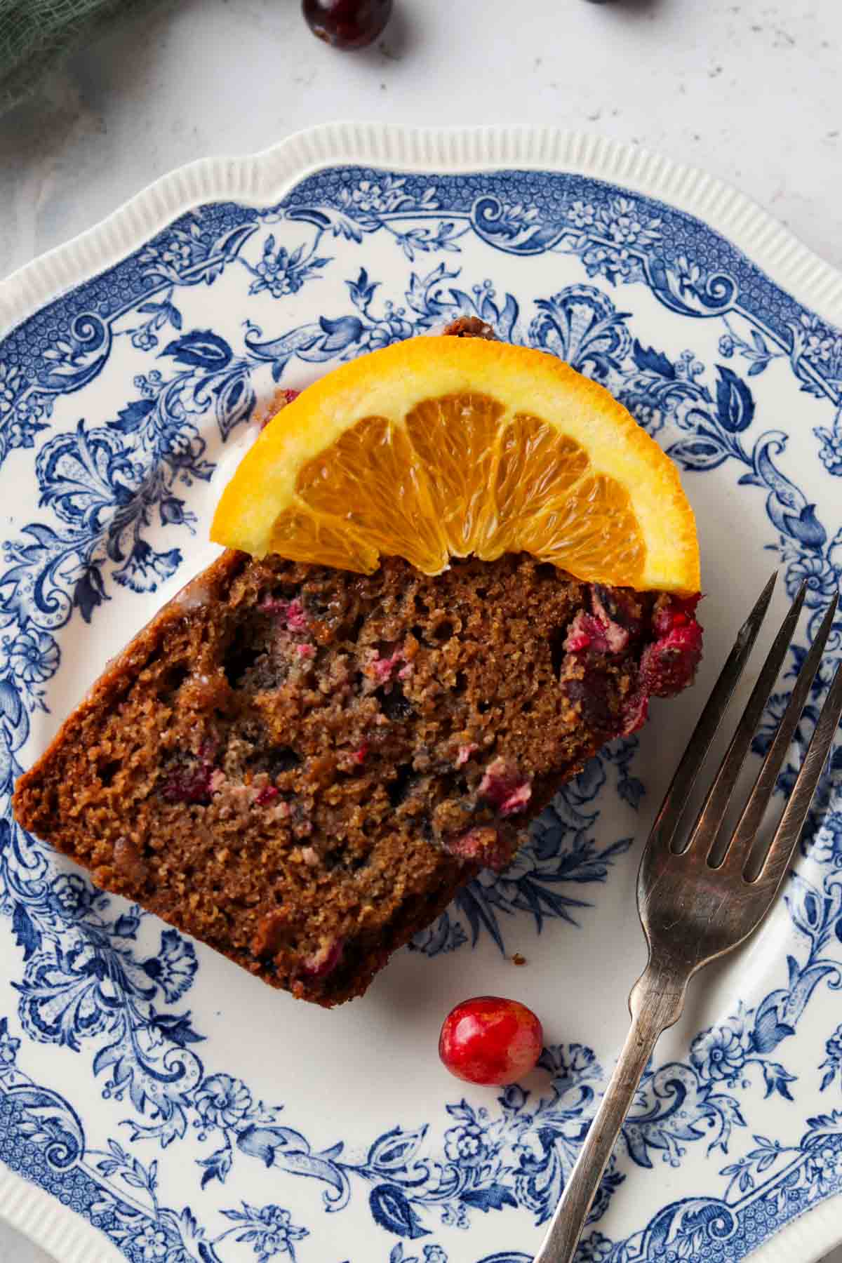 Piece of gluten free orange cake on a plate with an orange slice on top.