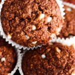 Close up photo of oat flour muffins stacked on top of each other with white chocolate chips on top.