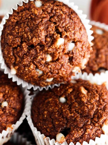 Close up photo of oat flour muffins stacked on top of each other with white chocolate chips on top.