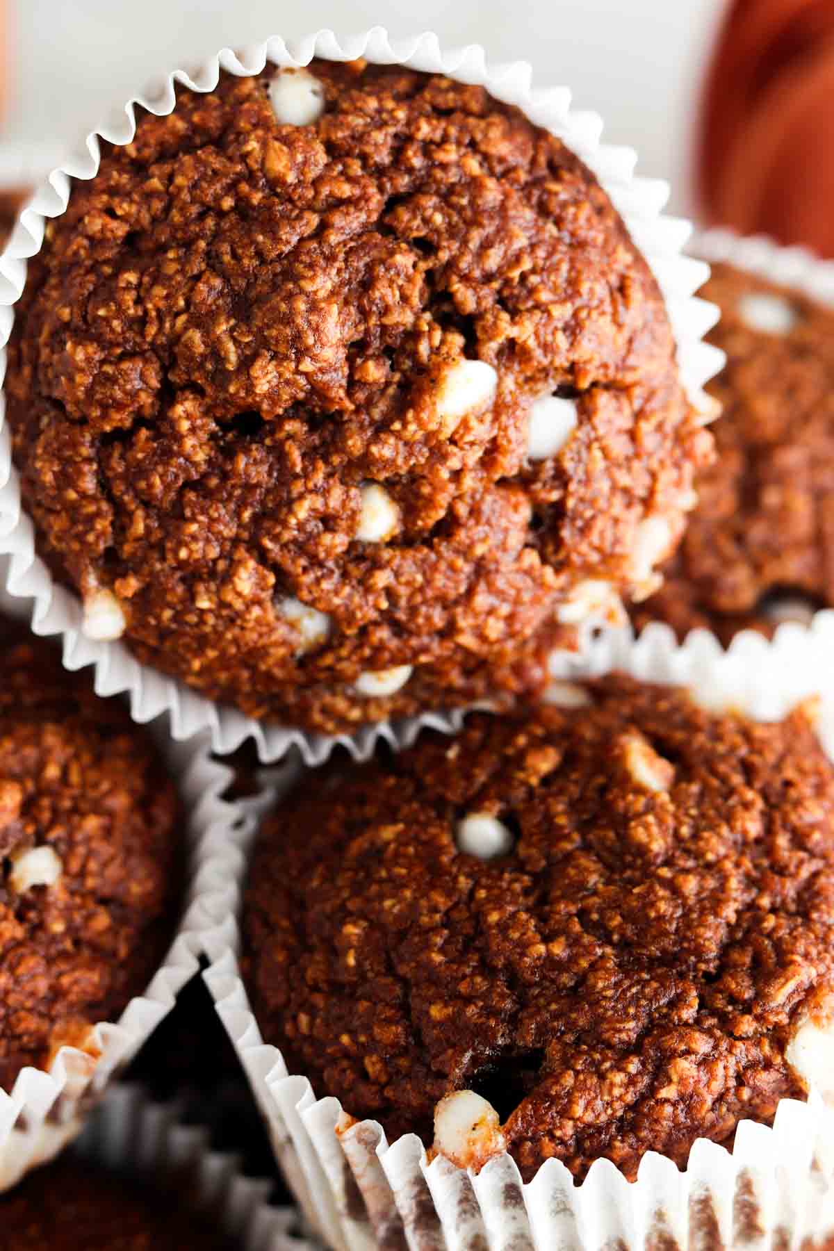 Close up photo of oat flour muffins stacked on top of each other with white chocolate chips on top.