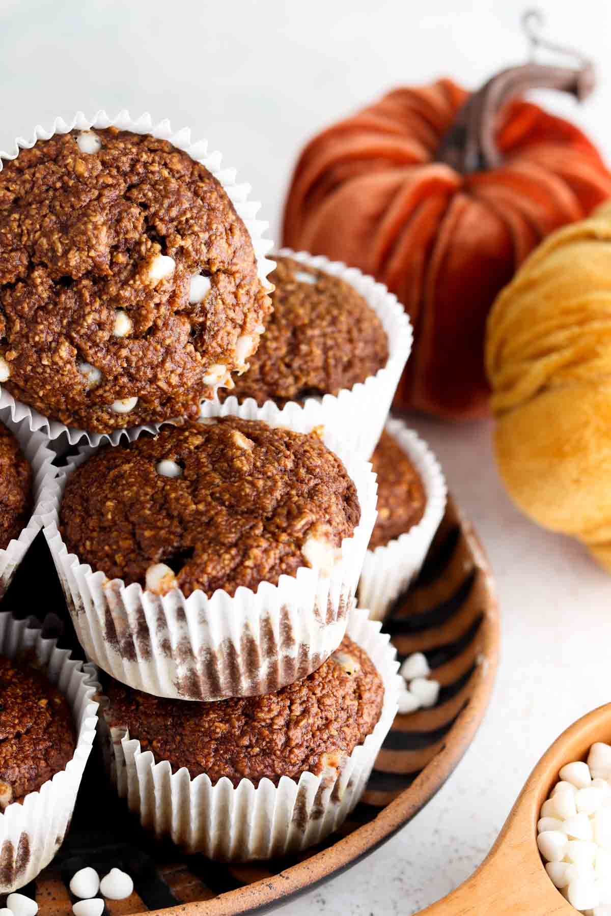 Pumpkin muffins with white chocolate chips stacked on each other with two pumpkins in the back.