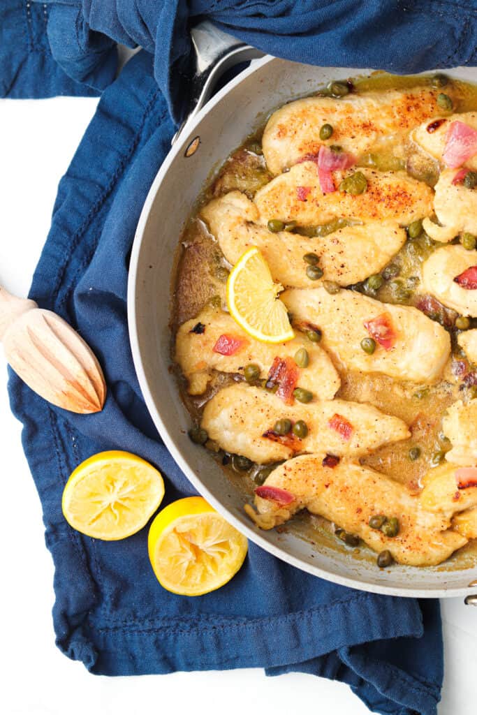 chicken piccata in a pan with lemon wedges 