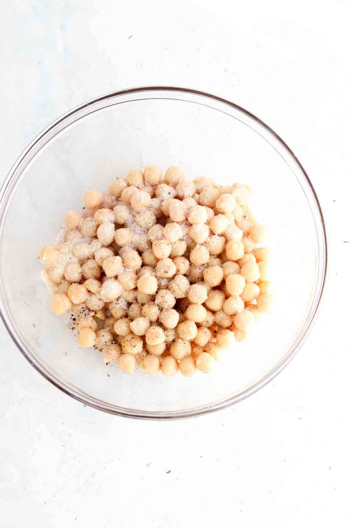 Chickpeas, oil and seasoning in a large glass bowl.