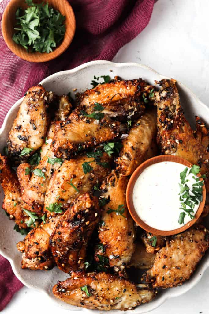 Everything bagel chicken wings in a bowl with a cup of garlic aioli on the side and fresh herbs sprinkled on top.