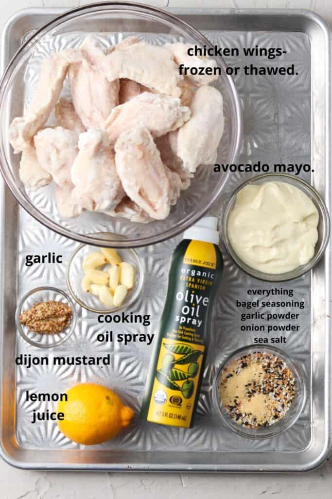 Chicken wings and aioli ingredients laid on in small glass bowls on a cookie tray. 