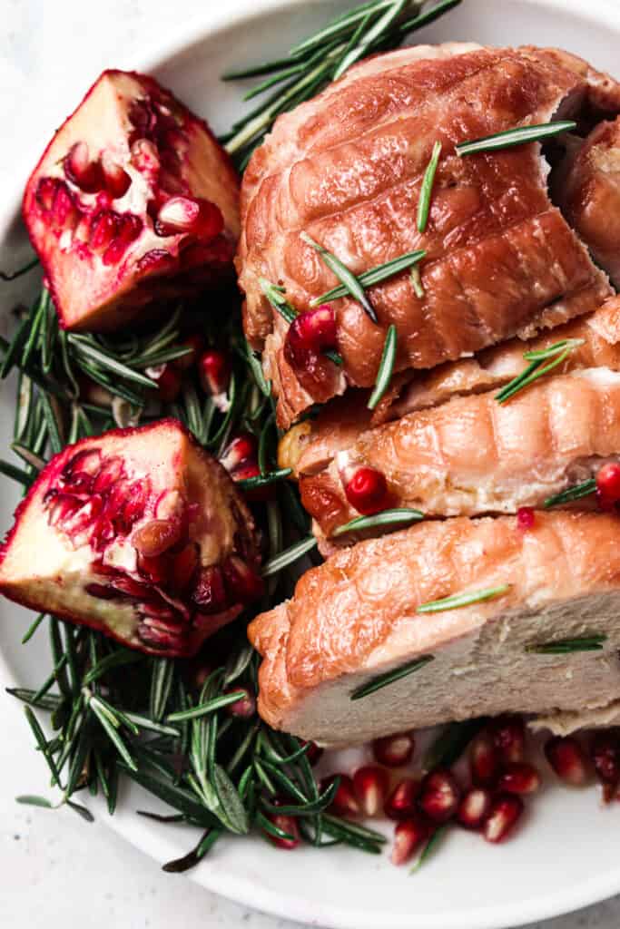 Beautiful photo of a boneless turkey breast on a plate with pomegranate and rosemary. 