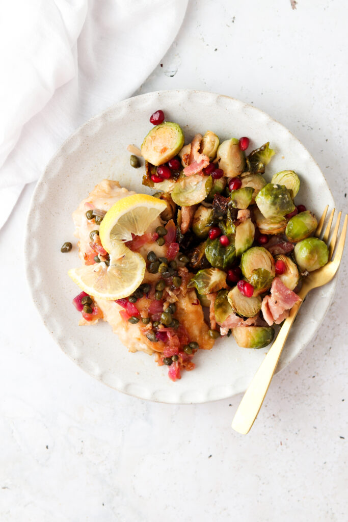 chicken piccata on a plate with lemons and brussel sprouts