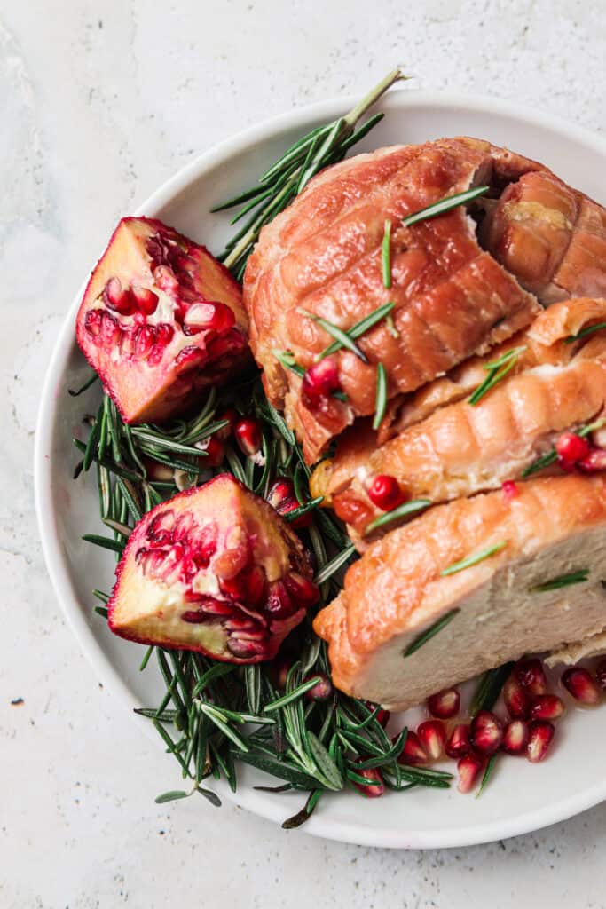 A roasted maple boneless turkey breast on a plate with rosemary and pomegranate. 
