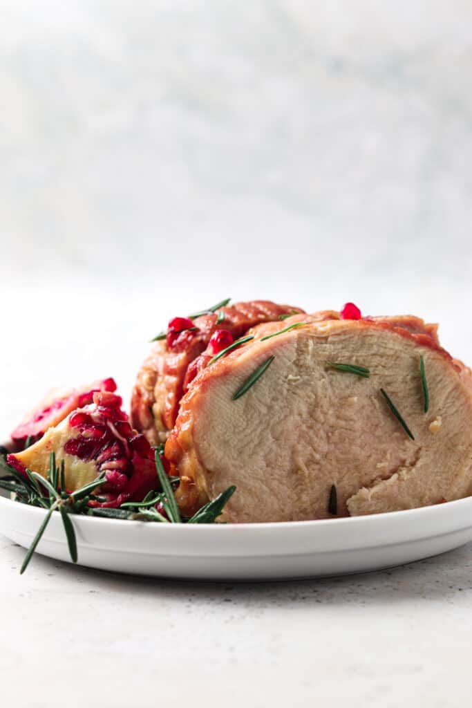 Side picture of turkey breast on a plate with fresh herbs. 