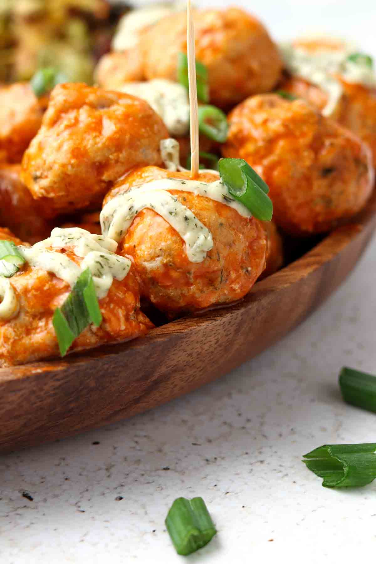 Buffalo chicken meatballs on a wooden platter with a toothpick in one.