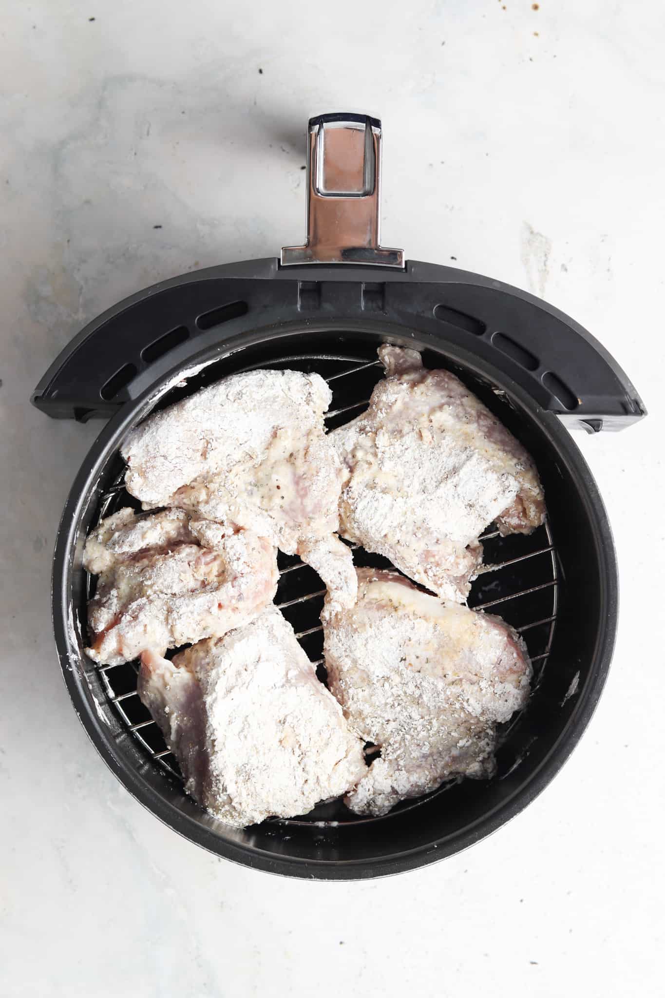 Breaded chicken thighs in an air fryer basket.