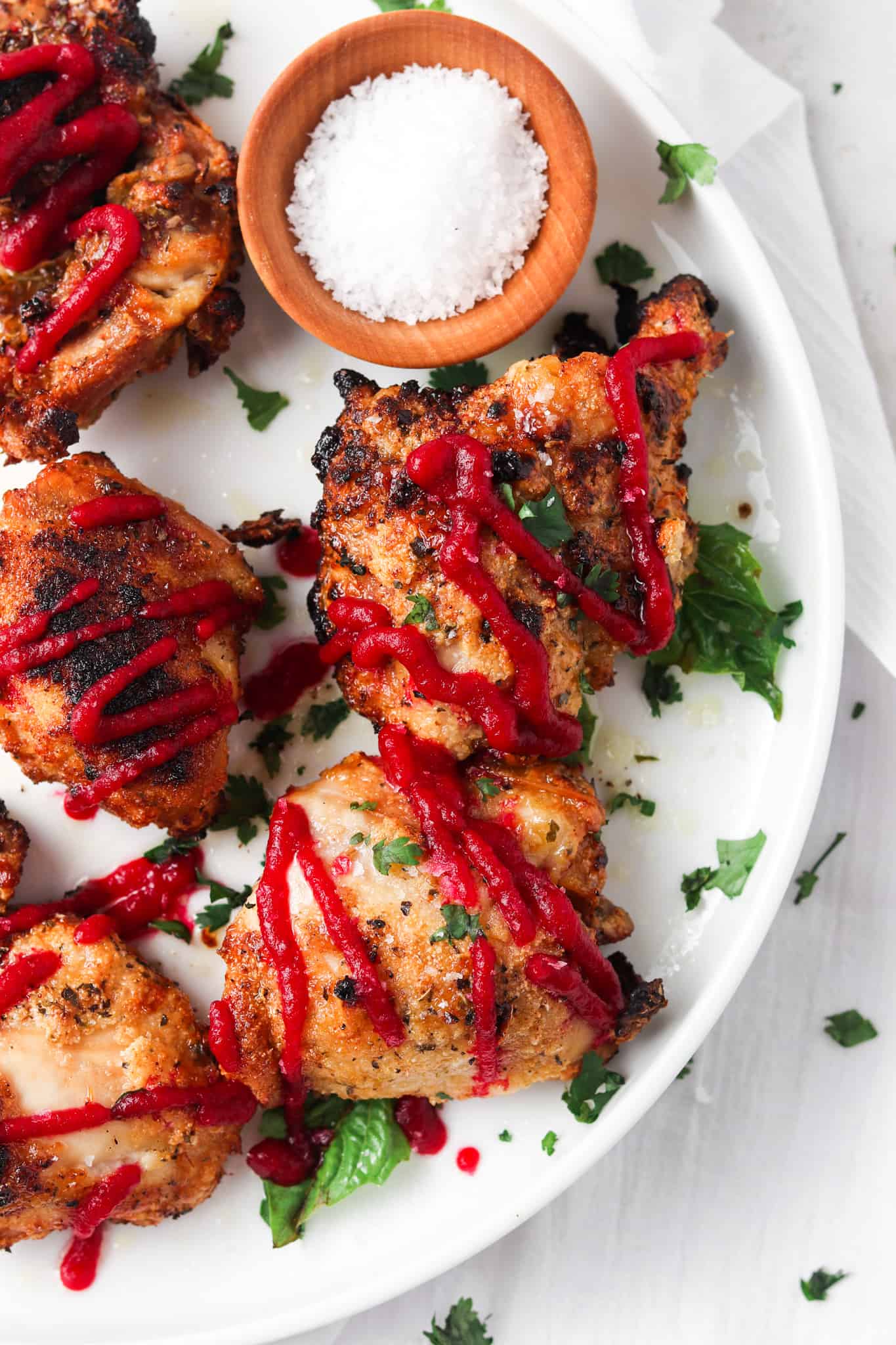 Crispy garlic aip chicken thighs on white plate with beet ketchup and a wooden bowl of sea salt.