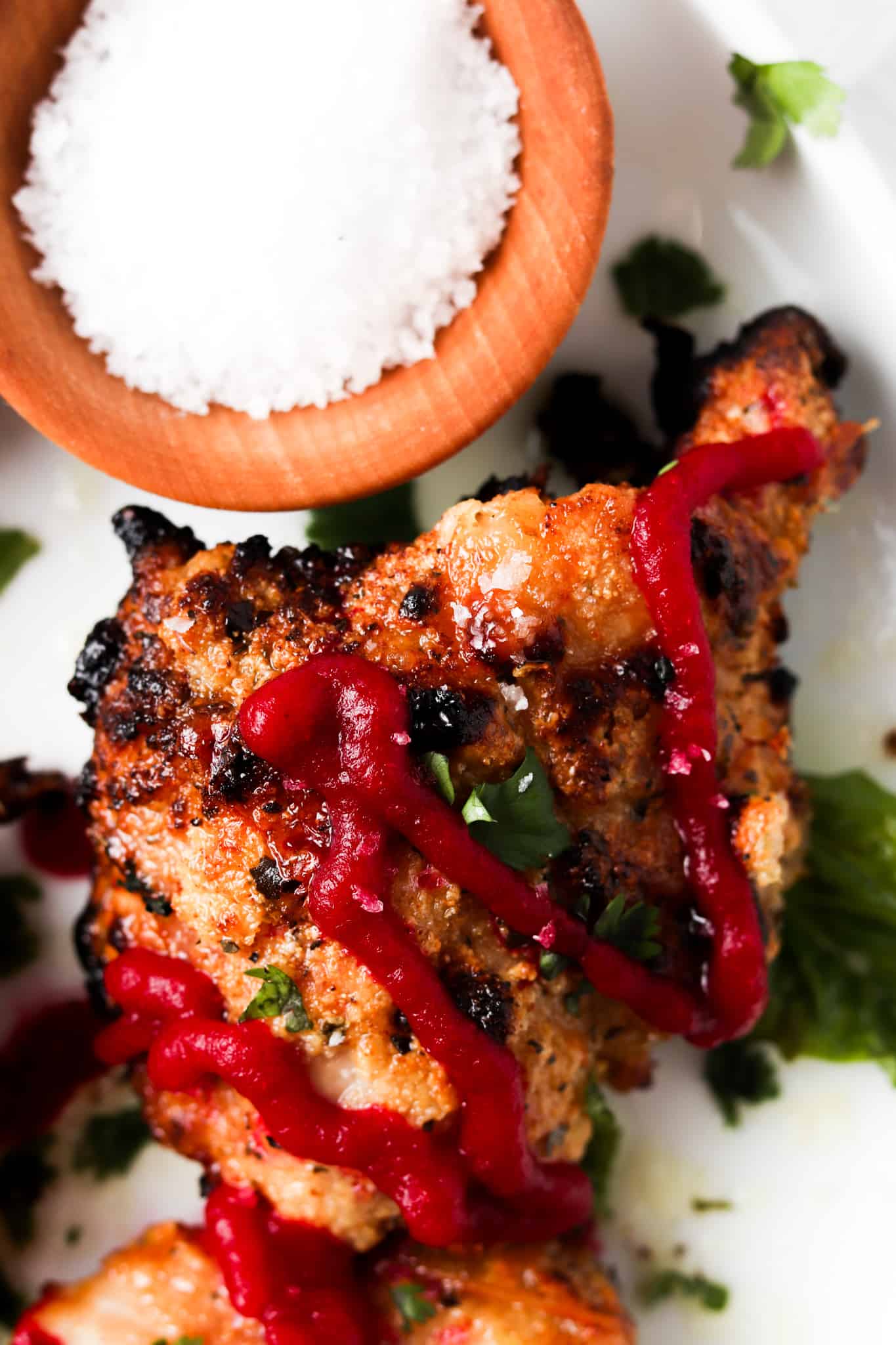 Very close up picture of crispy garlic aip chicken thighs with sea salt and beet ketchup on a white plate.