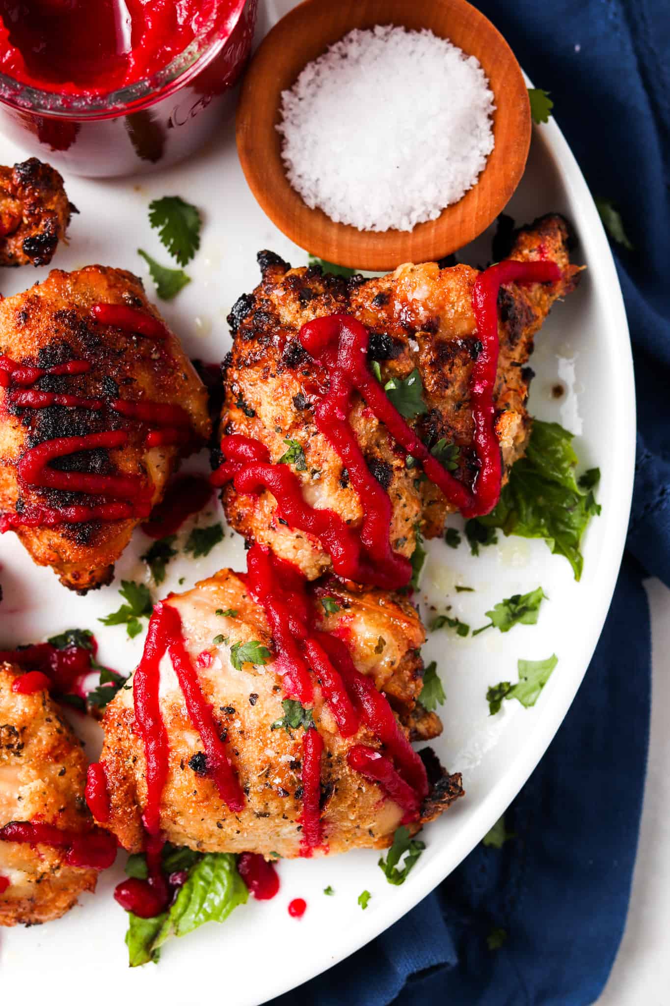 Crispy garlic aip chicken thighs on a while plate and garnished with fresh green herbs and aip beet ketchup.