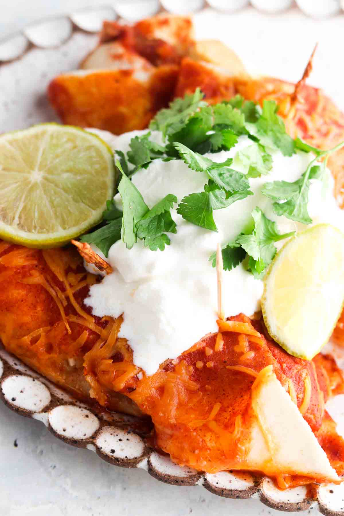 Two Enchiladas on a serving dish with fresh cilantro, dairy free sour cream and limes.