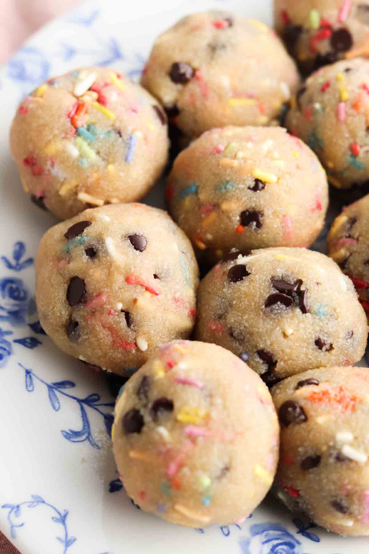 Cookie dough balls with rainbow sprinkles on a blue and white floral plate.