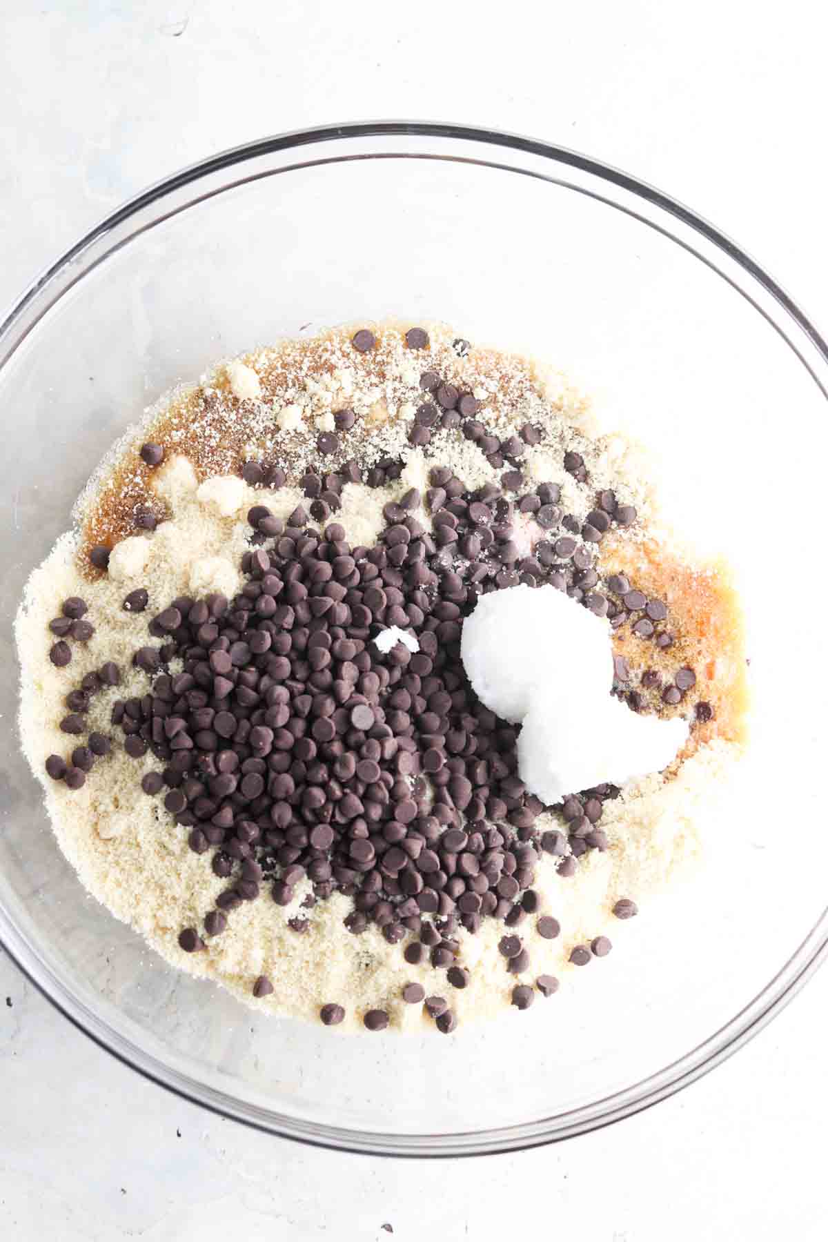Almond flour, chocolate chips, maple syrup, vanilla, and coconut oil in a large glass bowl.