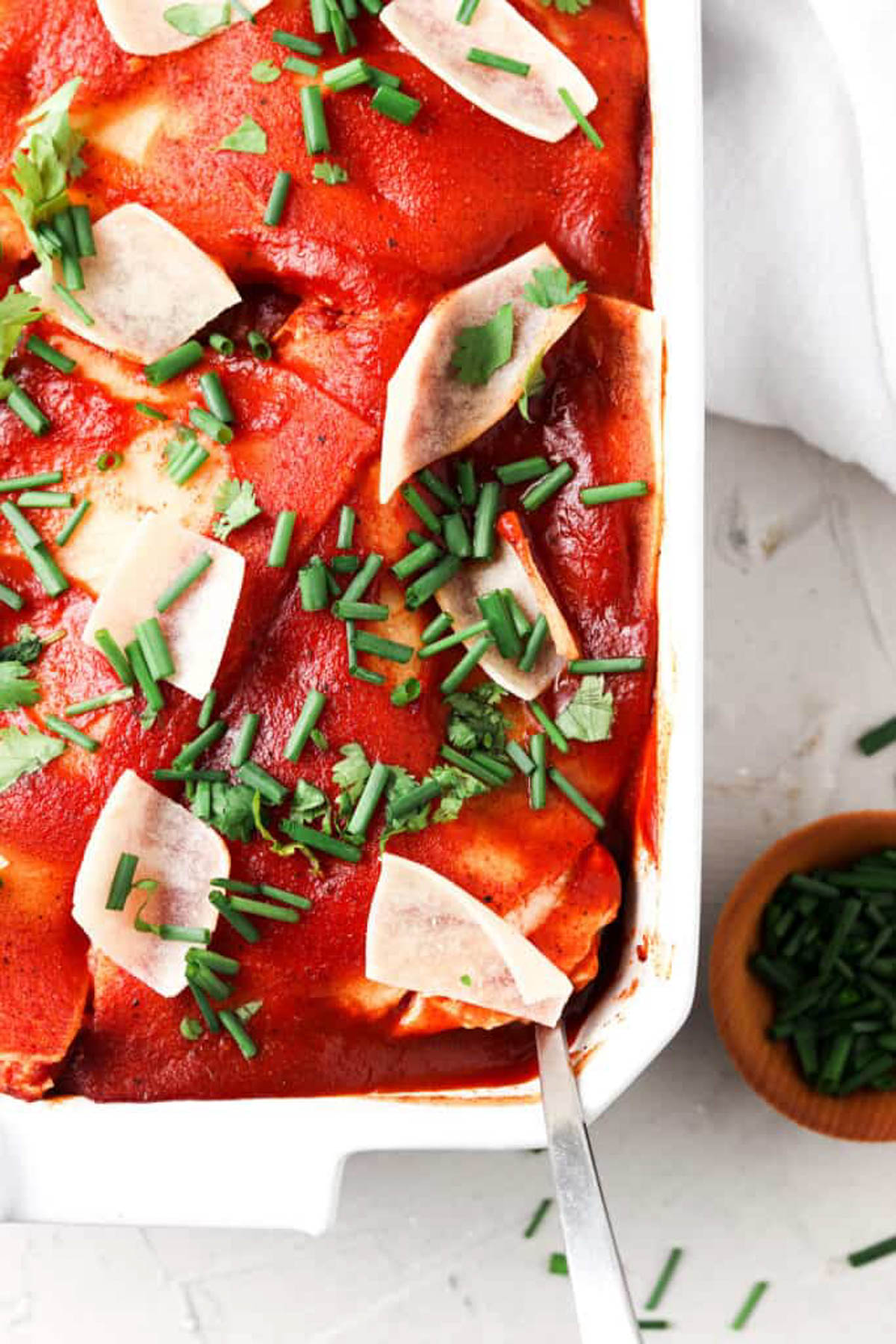 Dairy free enchiladas in a pan with fresh green herbs sprinkled on top.
