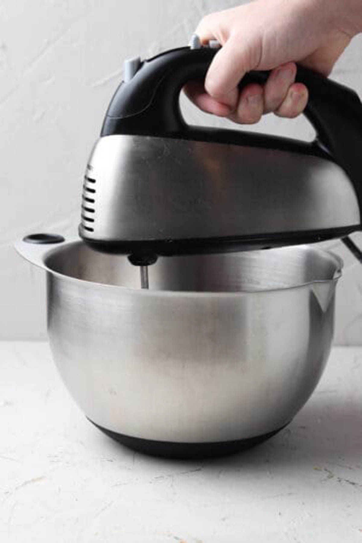 Chicken in a mixing bowl being shredded by a hand mixer for dairy free enchiladas.