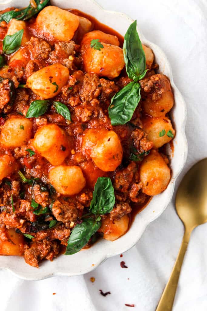 paleo gnocchi bolognese in a scalloped bowl with a gold spoon