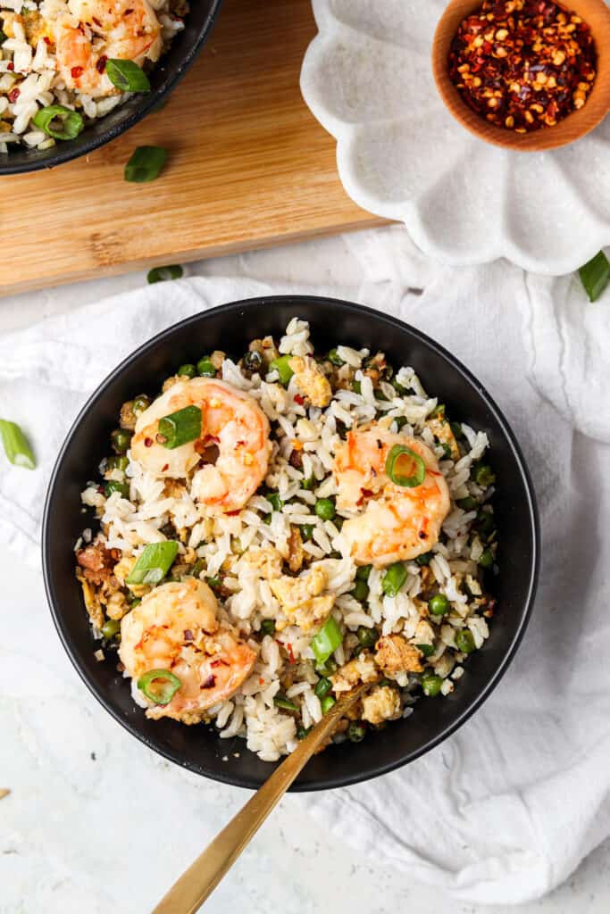 shrimp fried cauliflower rice in a black bowl with a spoon and red pepper flakes