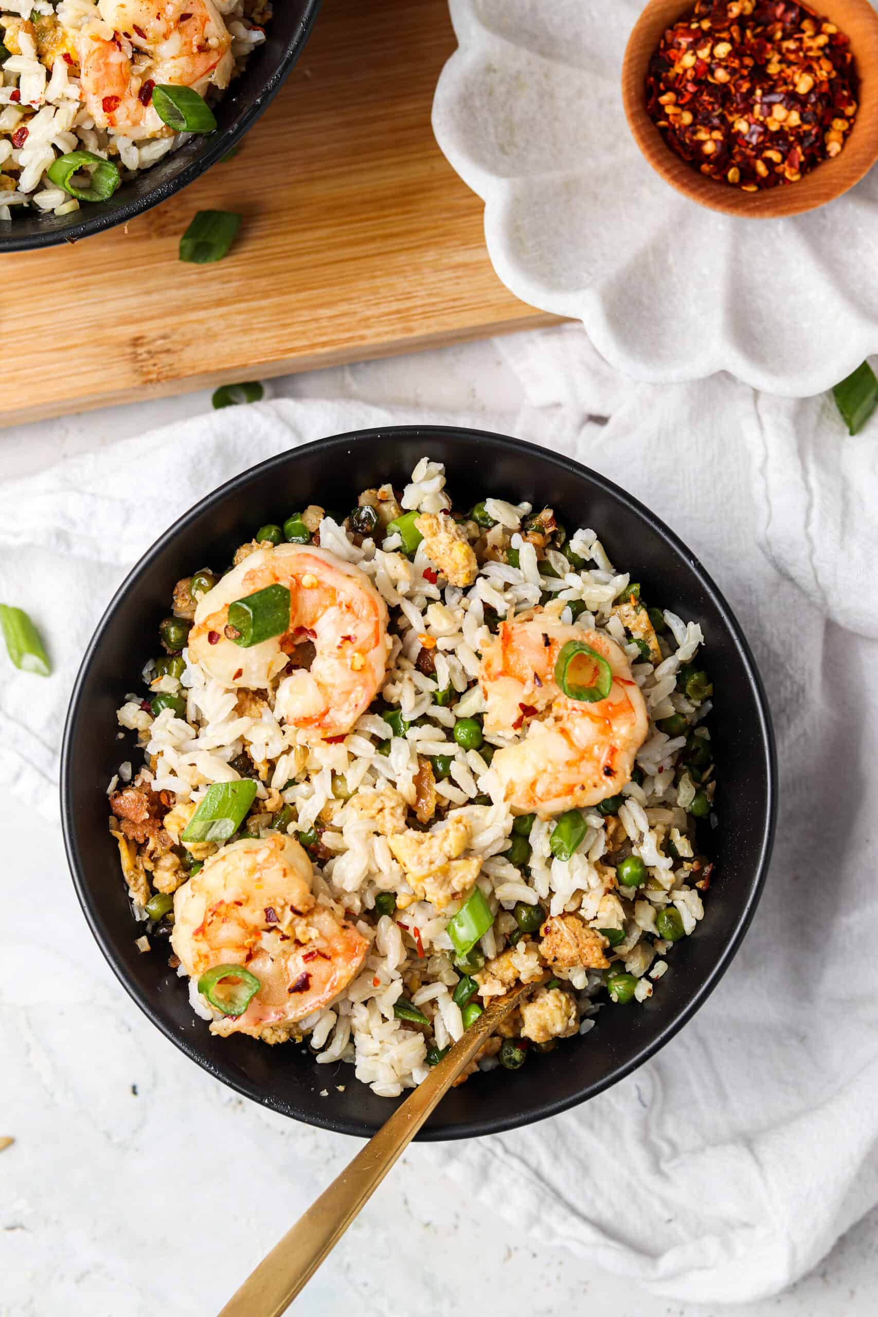 Shrimp fried cauliflower rice in a black bowl with a spoon and red pepper flakes.