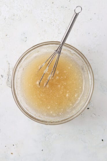 Gelatin egg mixture in a glass mixing bowl with a small whisk in it.