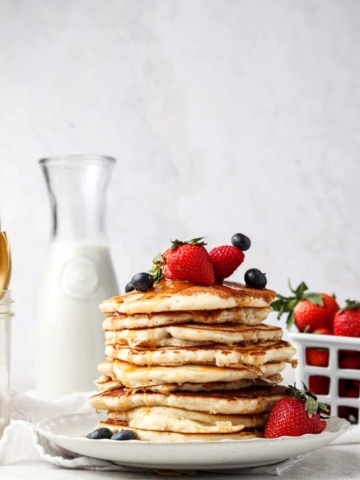 Stack of pancakes on a plate with fruit on top with maple syrup.