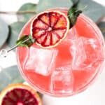 Overhead shot of a blood orange mojito in a glass with a dehydrated blood orange on the edge.