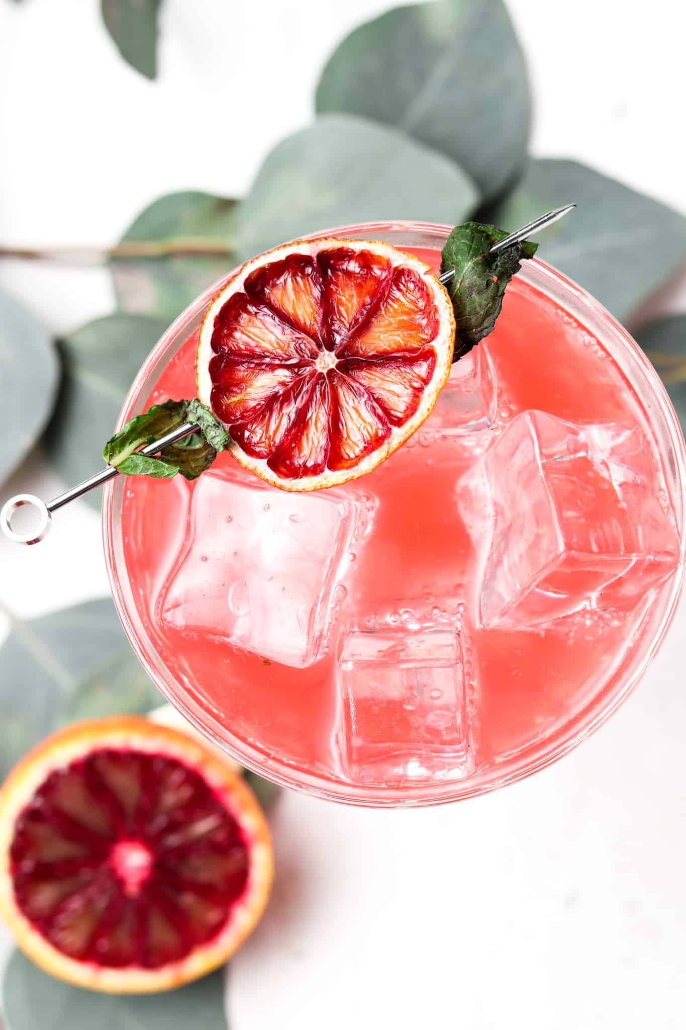 Overhead shot of a blood orange mojito in a glass with a dehydrated blood orange on the edge. 