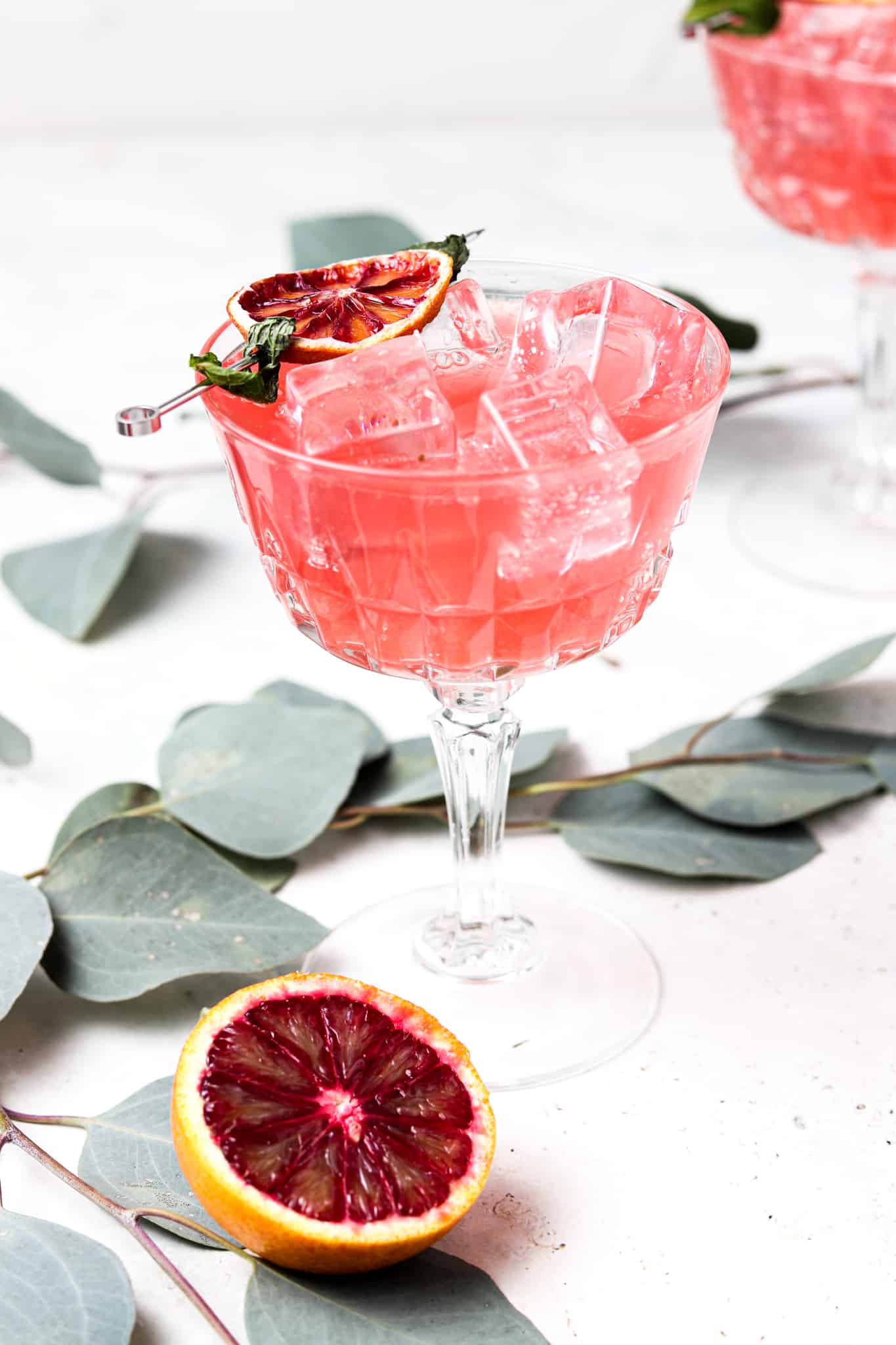 Side shot of an alcohol free blood orange mojito in a glass with mint and dehydrated blood orange garnishes on top.