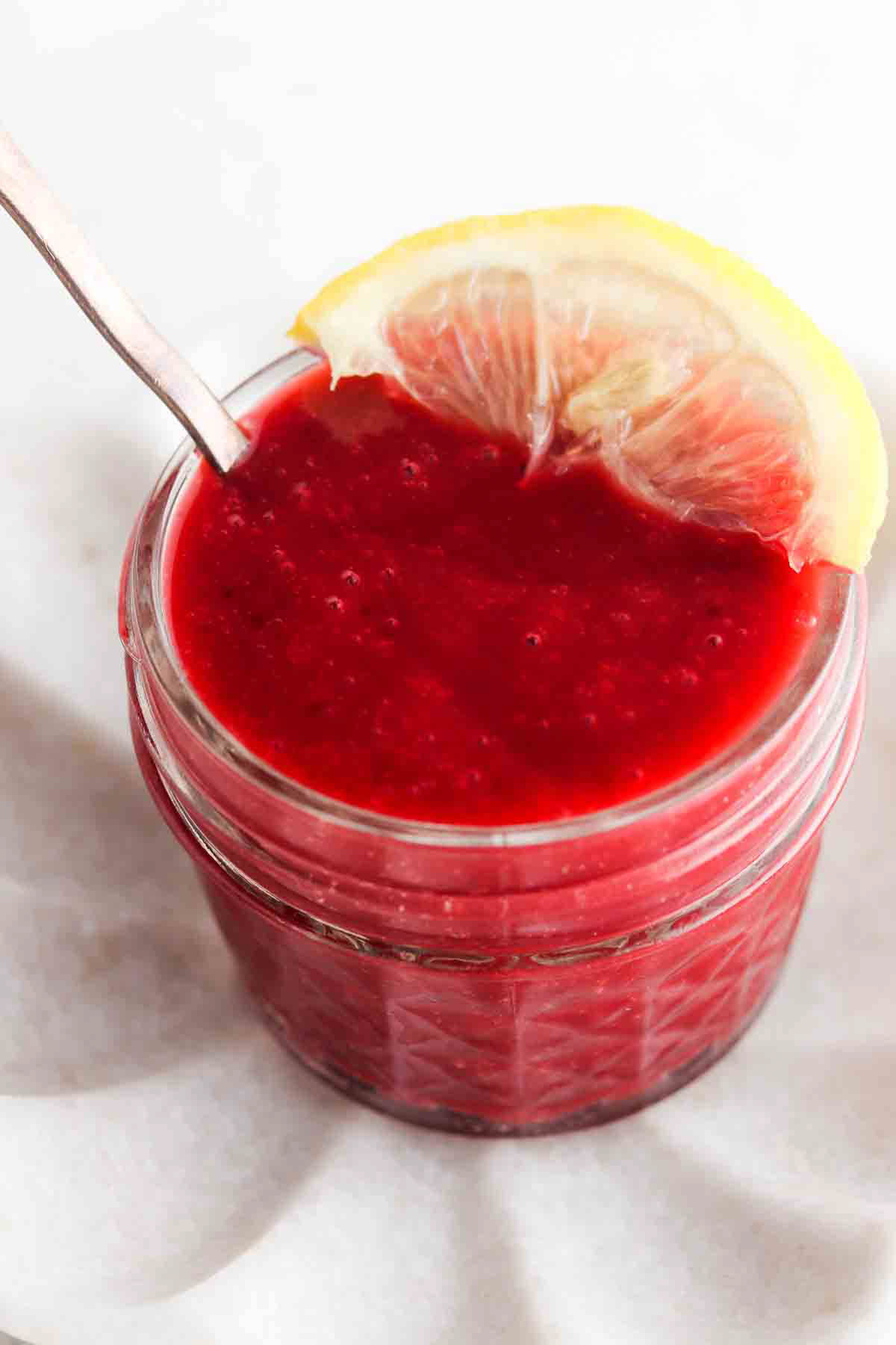 Raspberry jam in a small mason jar with a lemon on top.