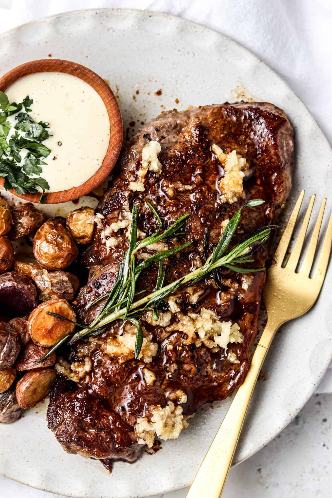 New york strip steak date night dinner on a white plate with garlic aioli and mini potatoes.