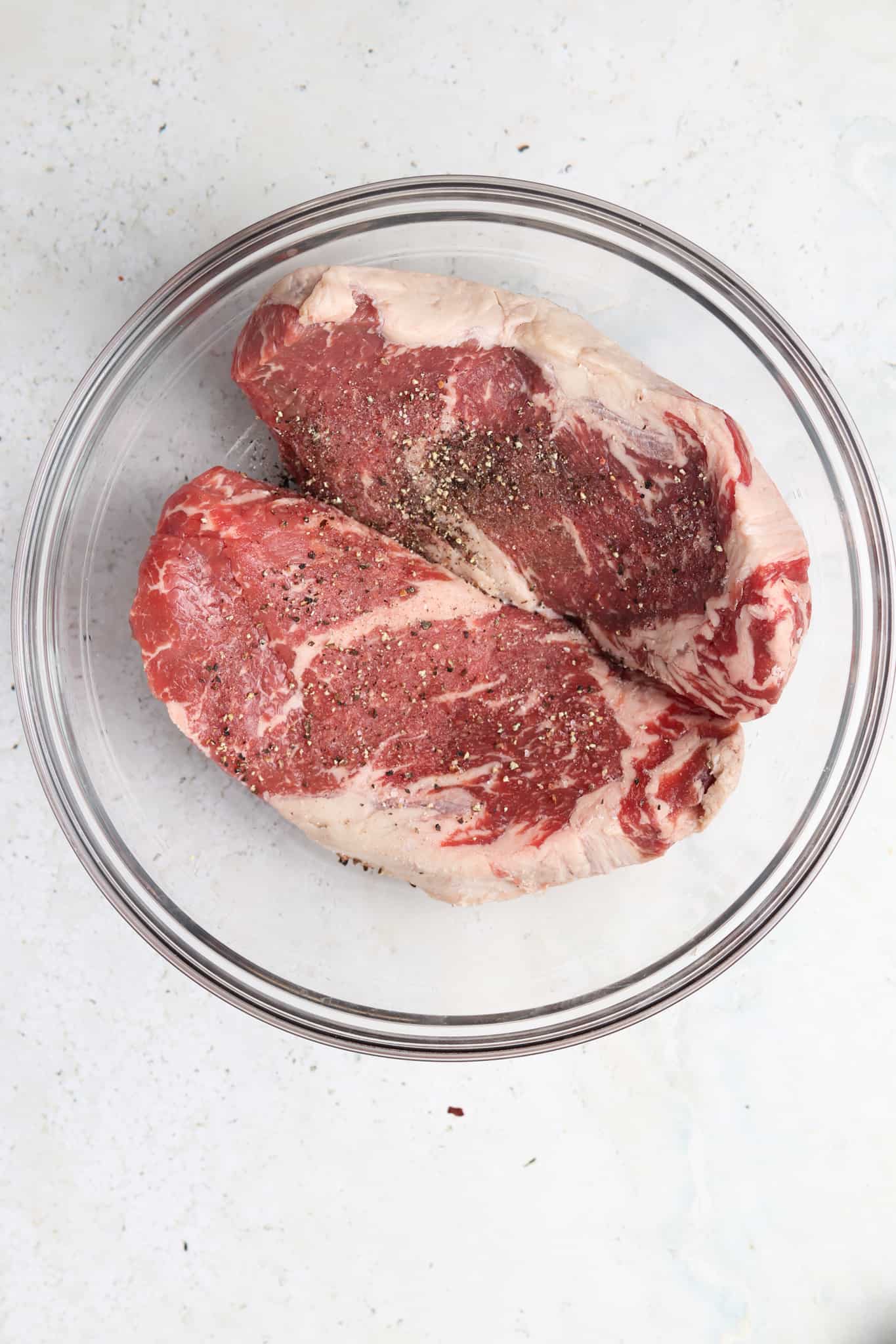 New york strip steak, garlic, sea salt, and black pepper in a glass mixing bowl.