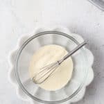 Gelatin and water in a glass mixing bowl with a small whisk.